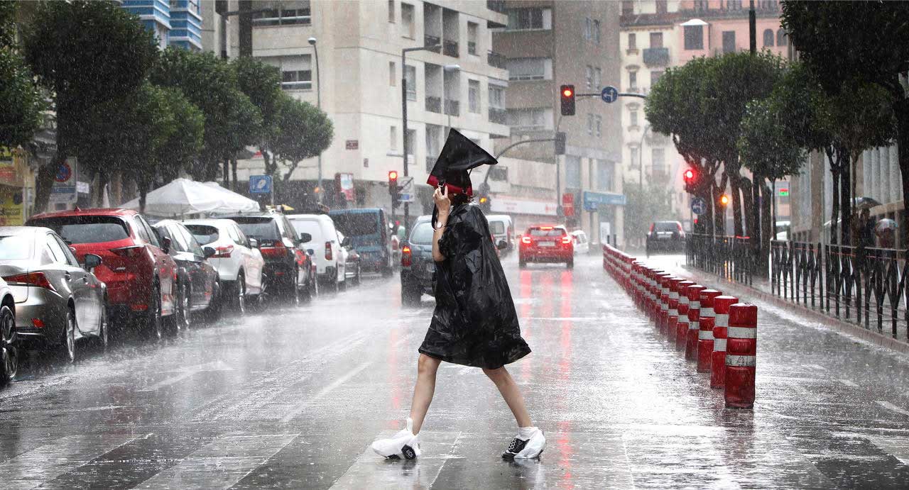 Una mujer cruza un paso de peatones, mientraqs llueve, cubierta por unas bolsas de plástico para no mojarse